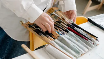 Hände organisieren Pinsel auf Holztisch.