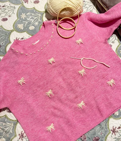 Rosa Pullover mit Stickerei, Garn und Reifen.