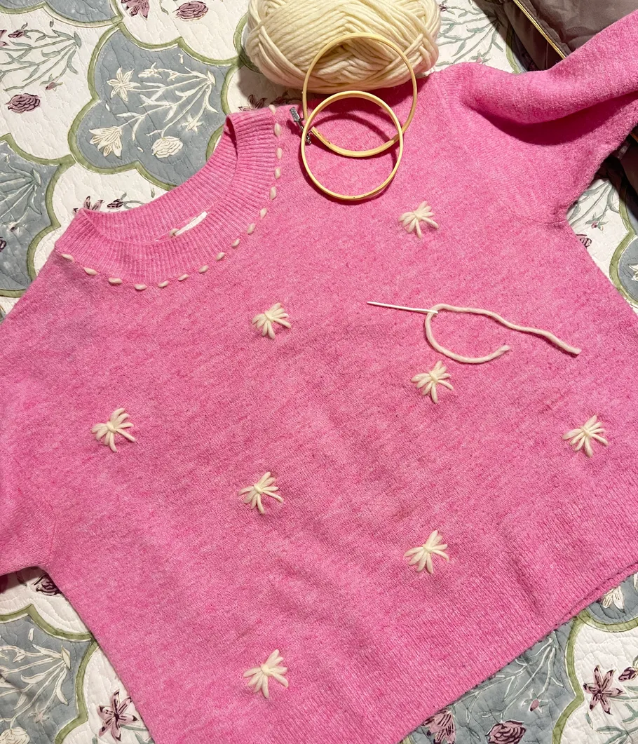 Pink sweater with embroidery, yarn, and hoops.