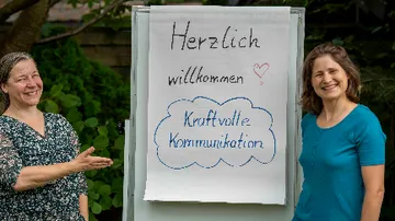 Two women present welcome sign outdoors.