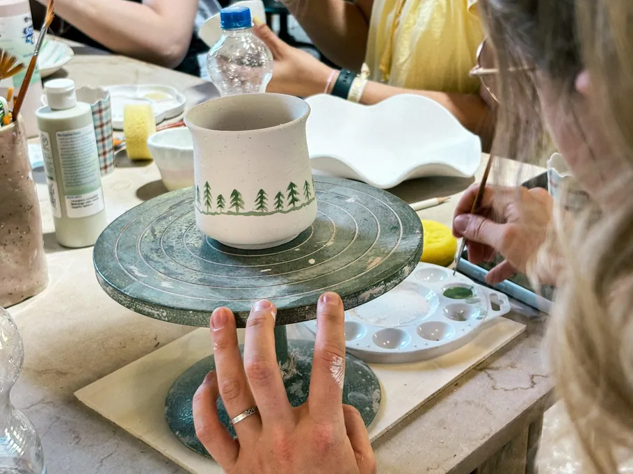 Person bemalt Tasse auf Töpferscheibe.