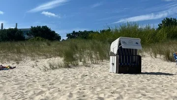 Beach chair on sandy beach, grassy dunes.