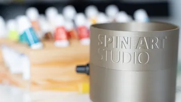 Metal cylinder labeled 'SPIN ART STUDIO' near paints.