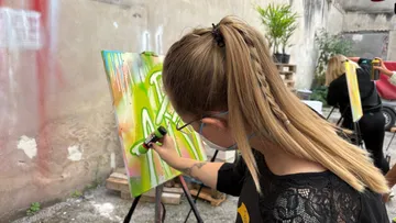 Woman spray painting on canvas outdoors.
