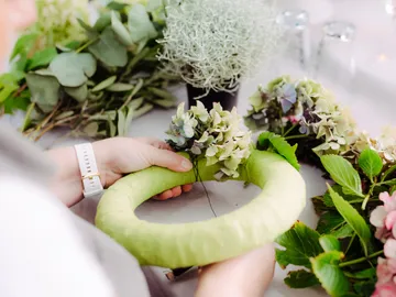 Person gestaltet einen Blumenkranz aus frischen Pflanzen.