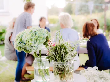 Flowers in vases stand at the table while people chat.