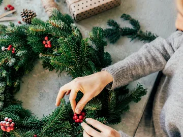 Hands decorate a wreath with berries on the table.