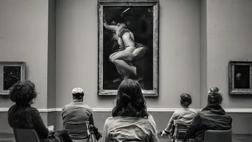 People sitting, viewing artwork in gallery.