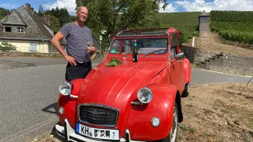 Red car parked, man holding drink roadside.