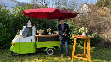 Man pouring wine by wine cart outside.