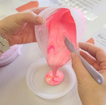 Hände gießen rosa Flüssigkeit in eine Form.