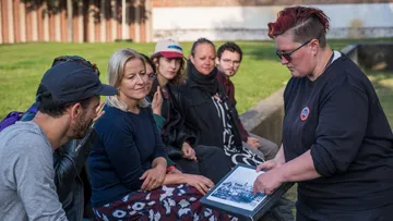 Person showing photo to seated group outdoors.