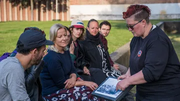Guide showing photo to seated group outdoors.