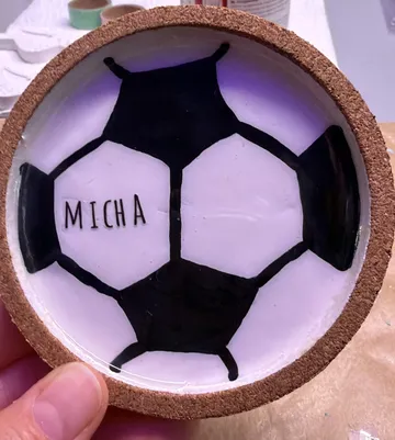 Hand hält Untersetzer mit Fußballmotiv.