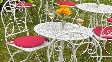 Weiße Gartenmöbel mit Weingläsern auf Gras.