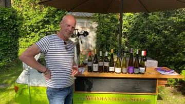 Mann genießt Wein an einem Weinstand draußen.