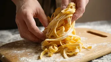 Hände formen Pasta auf Holzbrett.