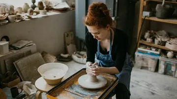 Woman shaping clay pottery in workshop.