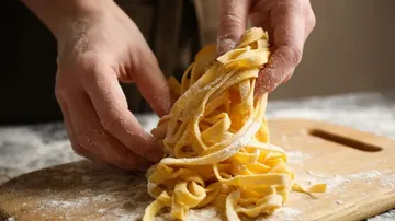 Hände formen frische Pasta auf Holzbrett.