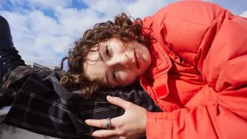 Person in red jacket rests on leg, outdoors.