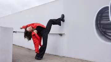 Woman in red jacket, bent pose, urban setting.