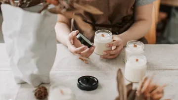 Person holding candle jars on table.