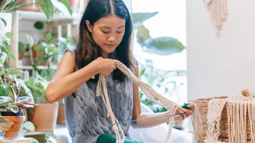 Person weaving yarn in a plant-filled room.