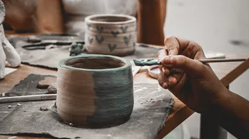 Hand painting a clay pot on table.