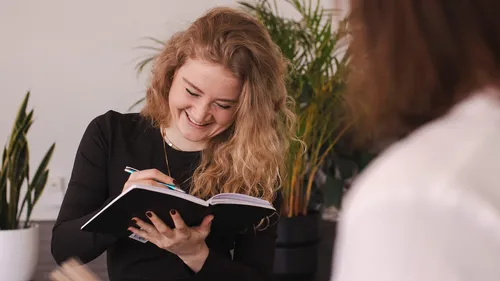 Woman writing in notebook, indoor plants.