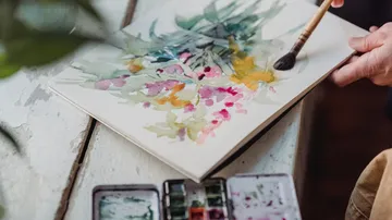 Hands painting colorful flowers with watercolors.