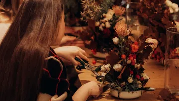 Person arrangiert Blumen an einem Holztisch.