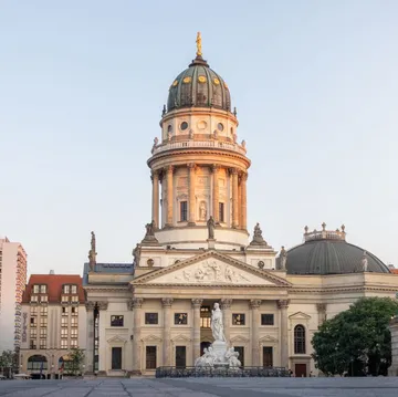 Historisches Kuppelgebäude mit Statuen, Stadtlandschaft im Hintergrund.