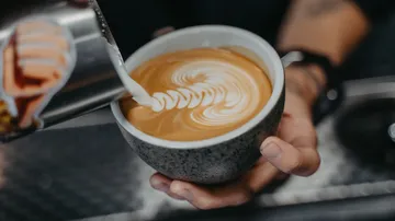 Coffee cup with latte art in barista's hand.