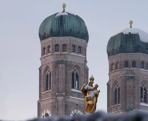 Goldene Statue vor zwei Kirchtürmen.