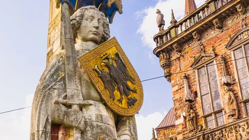 Steinfigur hält Schild neben historischem Gebäude.