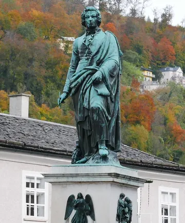 Statue eines Mannes vor herbstlichen Bäumen.