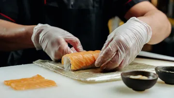 Chef rolls sushi on table.