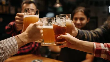 Hands clinking beer glasses in a bar.