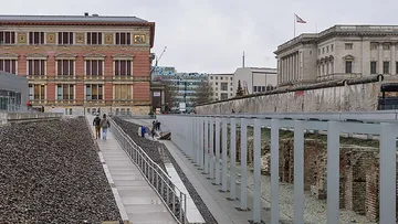 Menschen gehen neben Berliner Mauerresten.