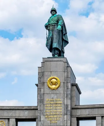 Statue Soldat steht auf Denkmal, bewölkter Himmel.