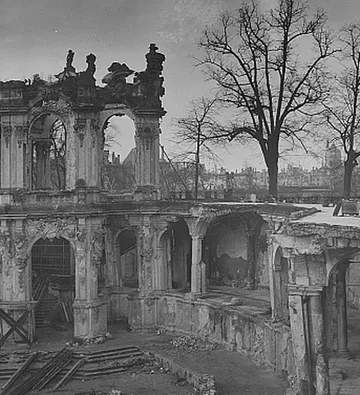 Ruined buildings amidst bare trees, dark sky.