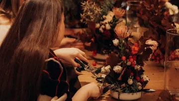 Frau arrangiert Blumen, sitzt am Tisch.