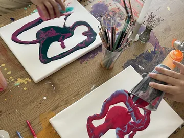 People pouring paint on canvases at table.