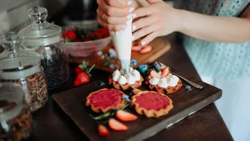 Hände verzieren Törtchen mit Sahne, Erdbeeren in der Nähe.