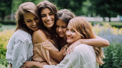 Vier Frauen umarmen sich lächelnd im Park.