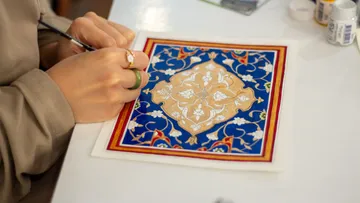 Person malt ein kompliziertes, buntes Design auf Papier.