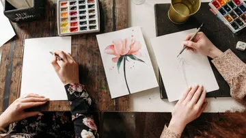 Zwei Personen zeichnen Blumen am Tisch.