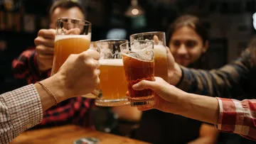 Hände stoßen Biergläser in einer Bar an.