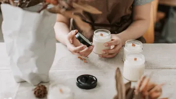 Person hält ein Glas mit Kerze auf Tisch.