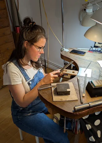 Frau fertigt Schmuck an einem Werktisch.